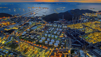 Aerial view of an oil refinery illuminated at night, showcasing its complex structures and glowing lights against the dark sky.